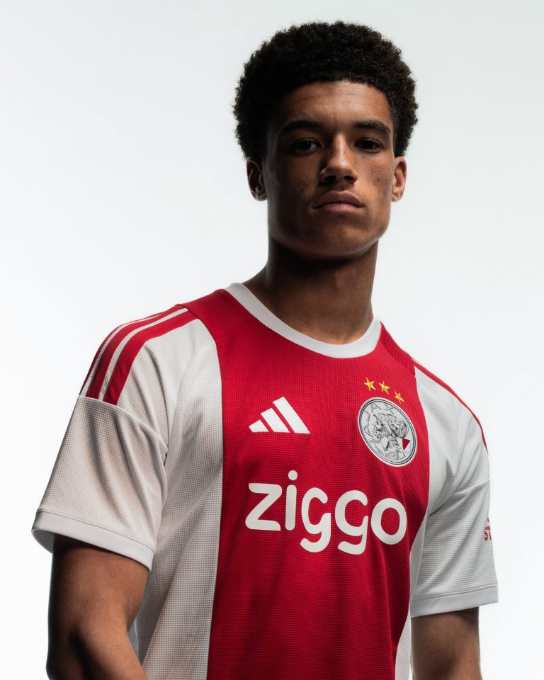 Een speler draagt het rood-witte thuisshirt van Ajax voor 2026-2027, met het clublogo en de sponsor Ziggo