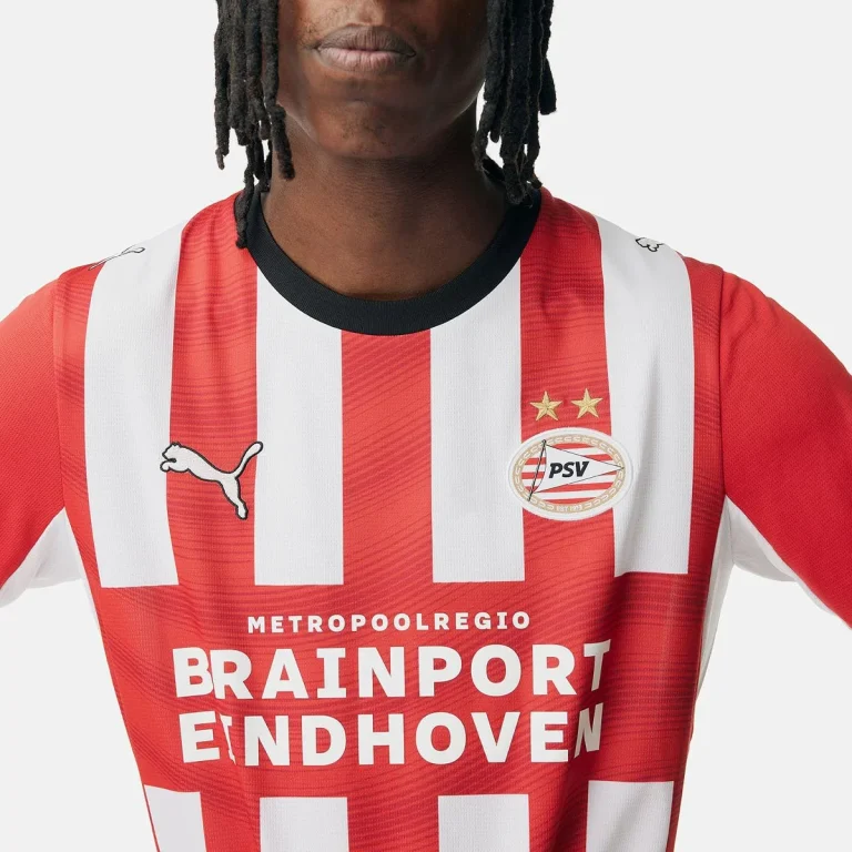 Close-up van het rood-wit gestreepte thuisshirt van PSV voor 2026-2027, met het clublogo en de sponsor Brainport Eindhoven