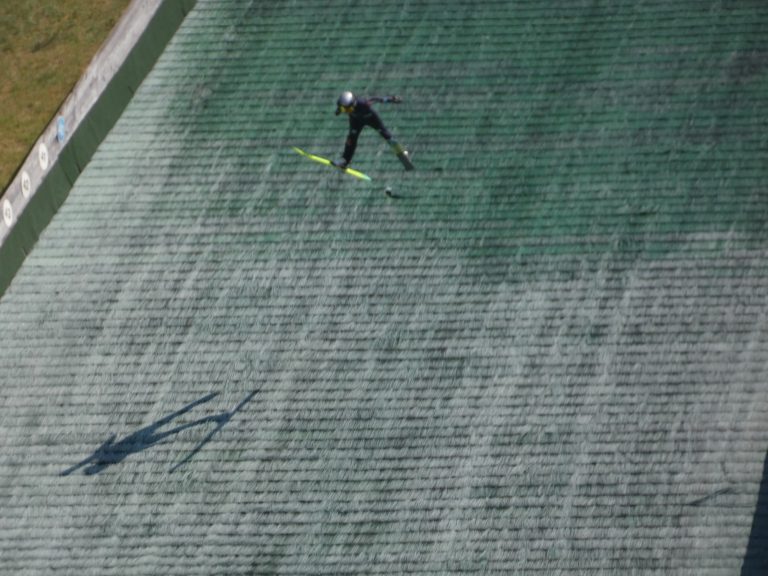 Een skispringer in volle vlucht boven het veld.